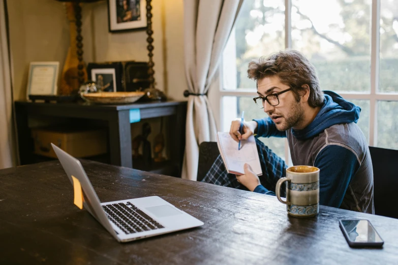 a man sitting at a table in front of a laptop, by Carey Morris, pexels contest winner, rhett and link, writing a letter, at home, people sitting at tables