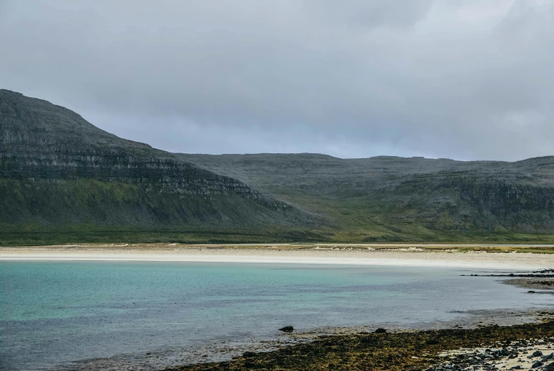 a body of water with mountains in the background, by Charlotte Harding, pexels contest winner, hurufiyya, orkney islands, beach is between the two valleys, a cozy, grey