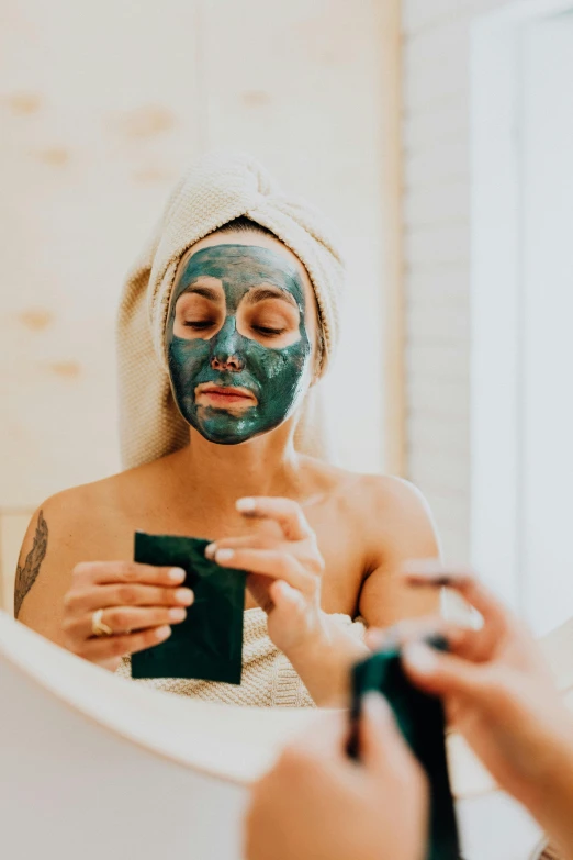 a woman getting a facial mask in front of a mirror, by Julia Pishtar, trending on pexels, wearing blue robe, green colored skin, charcoal skin, glitter
