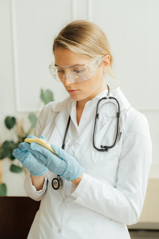 a woman in a lab coat and goggles holding a banana, a picture, shutterstock, analytical art, phone in hand, dissection relief, low quality photo, first aid kit