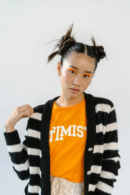 a woman standing in front of a white wall, an album cover, inspired by Kim Tschang Yeul, featured on reddit, toyism, wearing an orange t-shirt, striped sweater, resembling a mix of grimes, times magazine