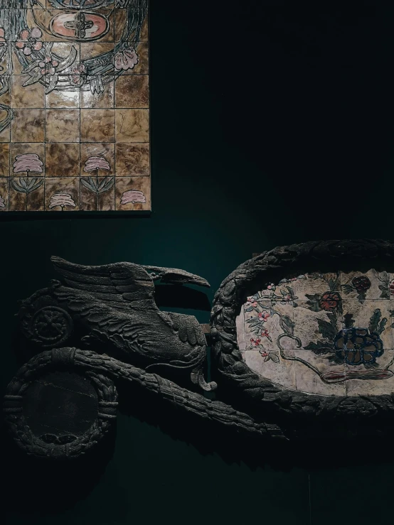 a motorcycle shaped bowl sitting on top of a table, an album cover, by Elsa Bleda, qajar art, ancient stone tiling, in a baroque museum exhibit, dark and moody aesthetic, angel relief