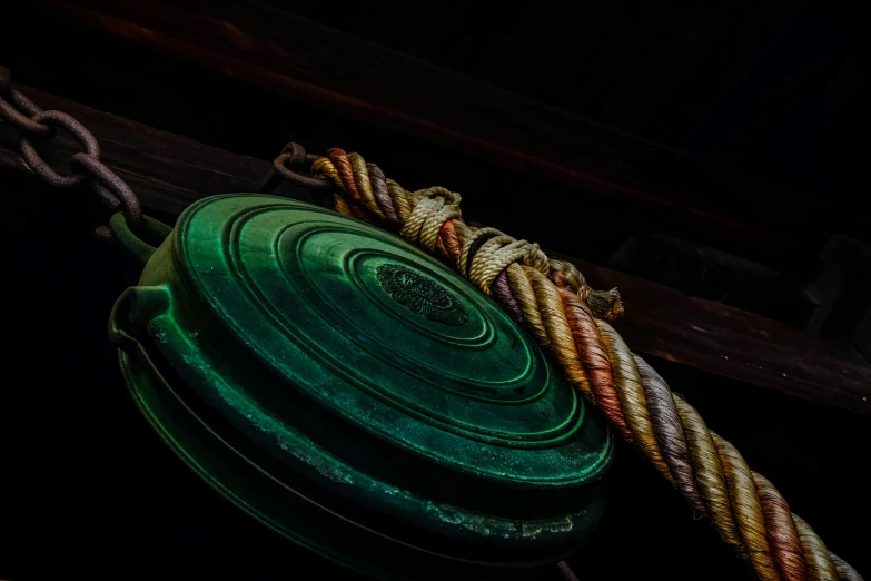 a green pulley sitting on top of a wooden pole, pexels contest winner, art photography, copper and emerald inlay, on ship, dark setting, multi - coloured