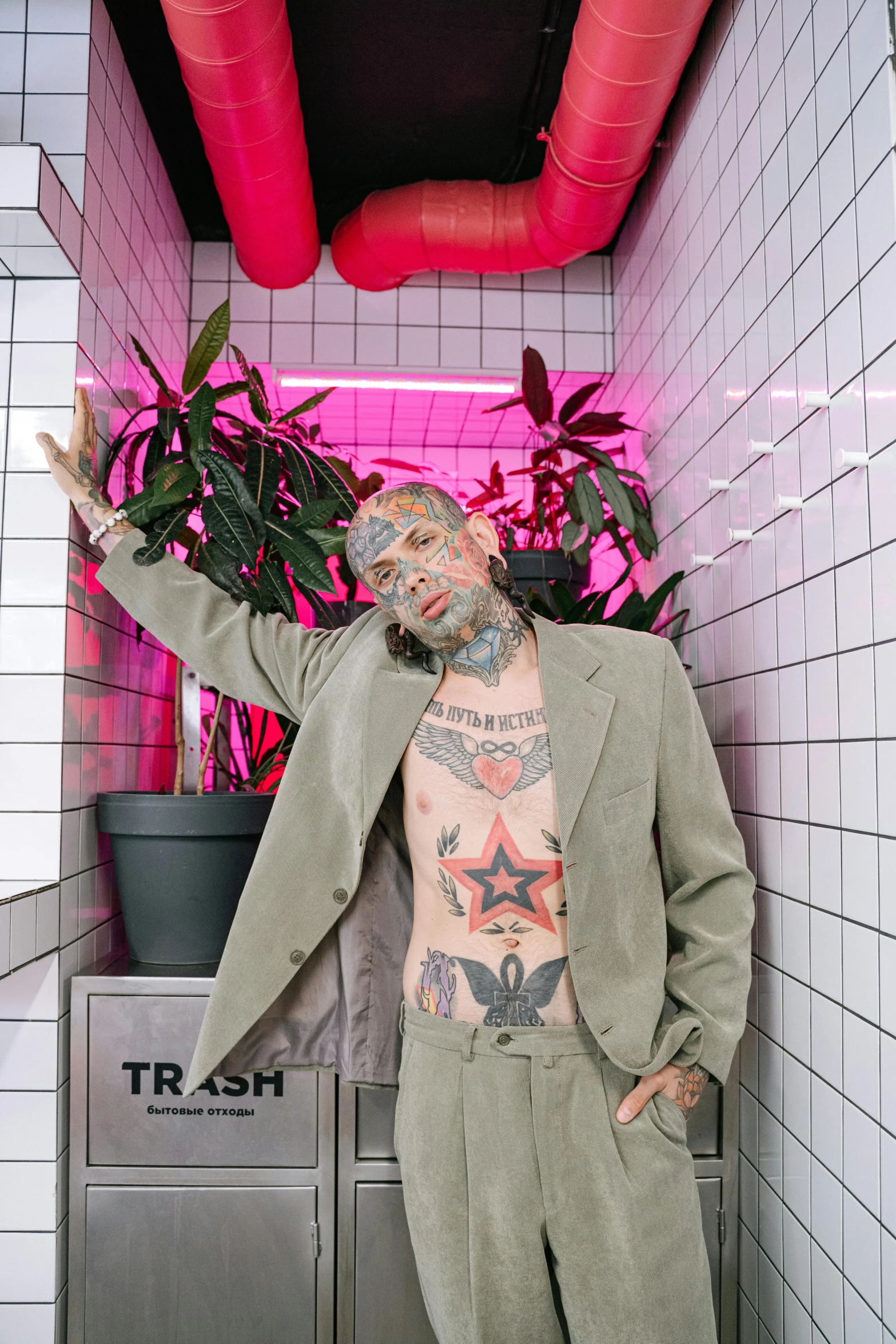 a man standing in a bathroom next to a plant, an album cover, inspired by James Bolivar Manson, trending on pexels, graffiti, tan suit, lil peep, fully tattooed body, old man