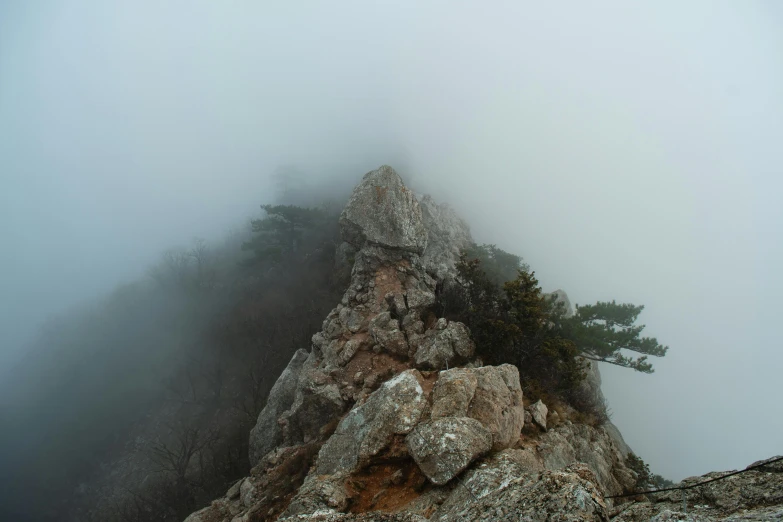 a person standing on top of a mountain on a foggy day, a picture, by Jang Seung-eop, unsplash contest winner, romanticism, jagged rocks, close up shot from the top, gray fog, today\'s featured photograph 4k