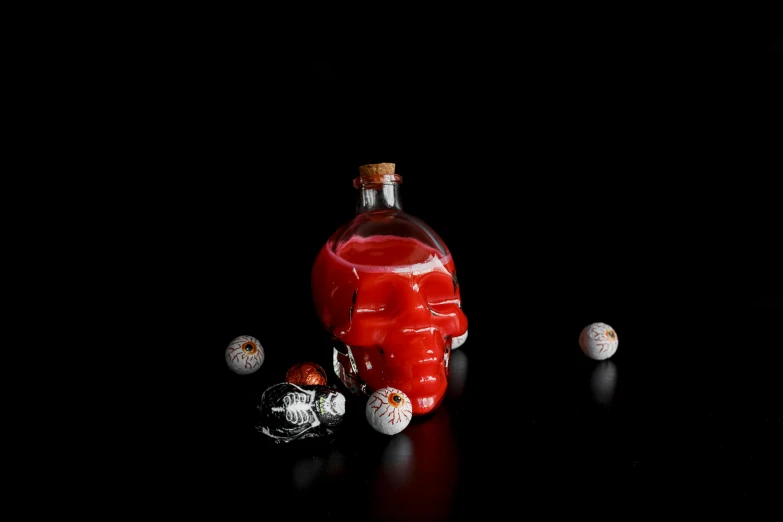 a bottle of liquid sitting on top of a table, vanitas, nose of red skull, on black background, alien skulls, made of glazed