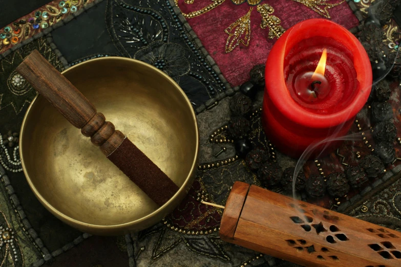 a singing bowl sitting on top of a table next to a lit candle, miscellaneous objects, maroon, brass, black