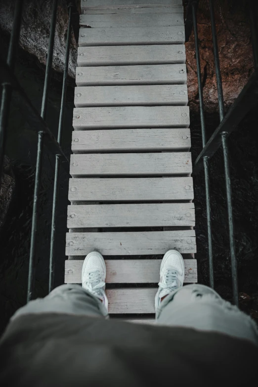 a person standing on a wooden bridge, wearing white sneakers, stairways, down there, unsplash photography