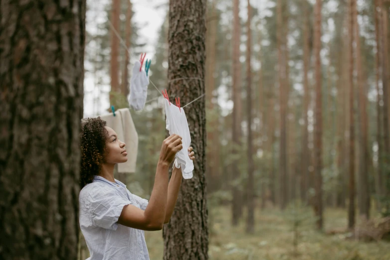 a woman flying a kite in a forest, by Emma Andijewska, pexels contest winner, environmental art, laundry hanging, african american young woman, holding a white flag, maintenance photo