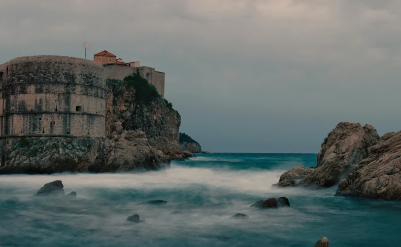 a castle sitting on top of a cliff next to the ocean, by Matija Jama, pexels contest winner, renaissance, overcast dusk, hd footage, turbulent sea, split near the left