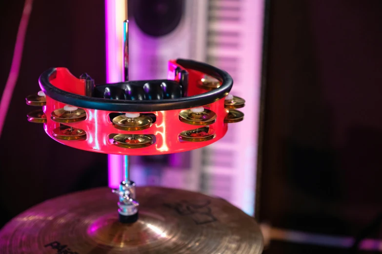 a musical instrument sitting on top of a drum, by Julia Pishtar, kinetic art, red and obsidian neon, middle close up shot, studio lights, bangles