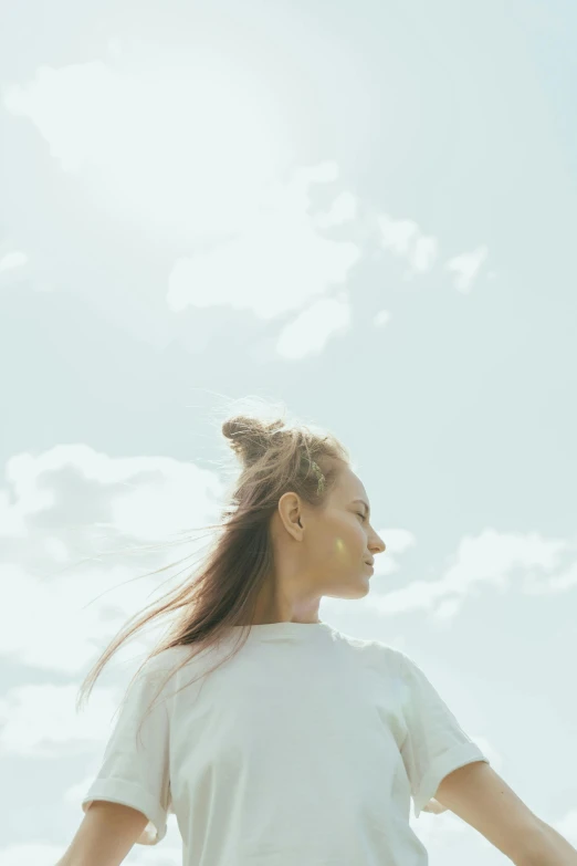 a woman standing on top of a lush green field, a picture, unsplash, hair styled in a bun, white sky, angle profile portrait, sunlit sky