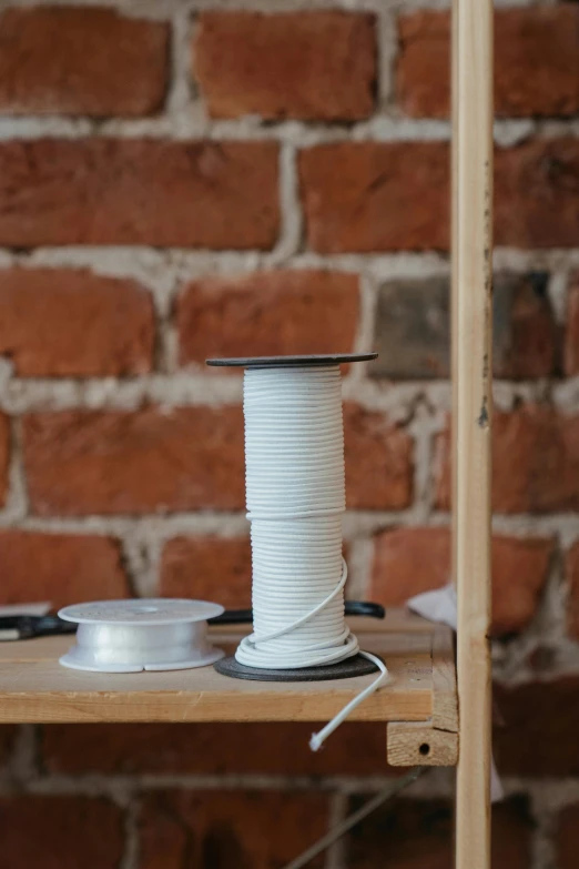 a spool of thread sitting on top of a wooden shelf, inspired by W. Lindsay Cable, white steel, electrical details, webbing, product image