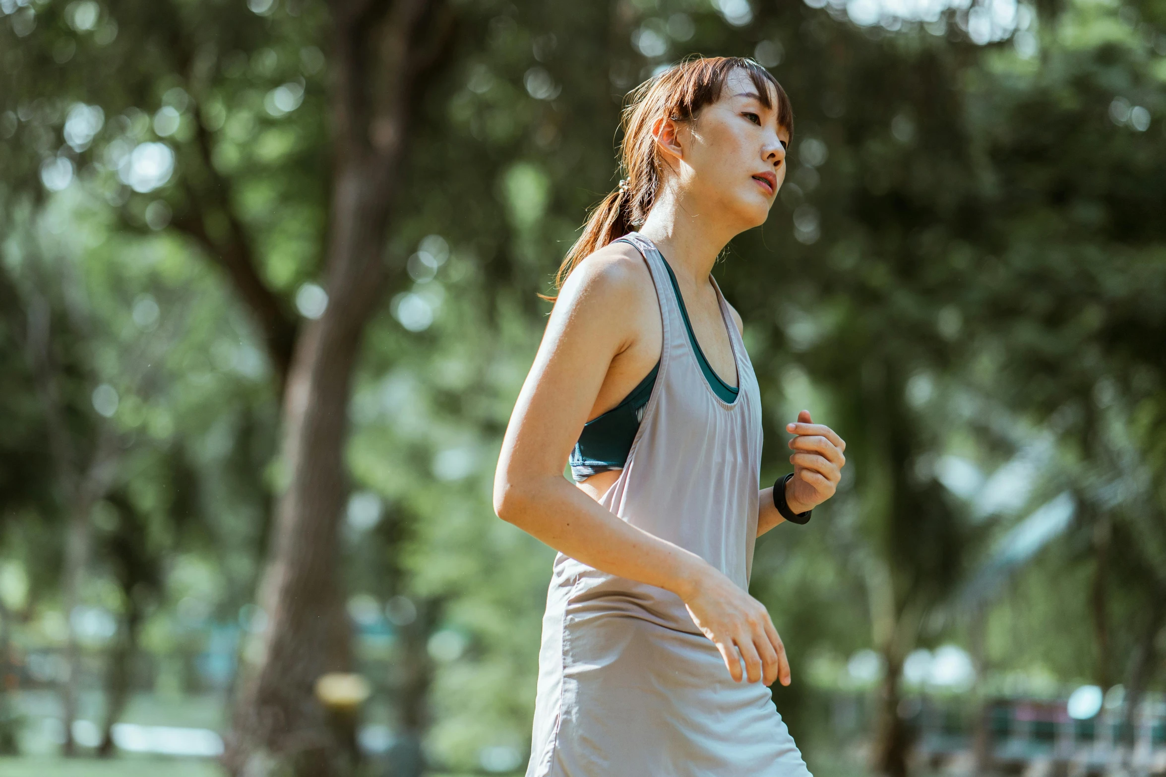 a woman running in a park with trees in the background, pexels contest winner, happening, wearing : tanktop, young asian woman, thumbnail, gray