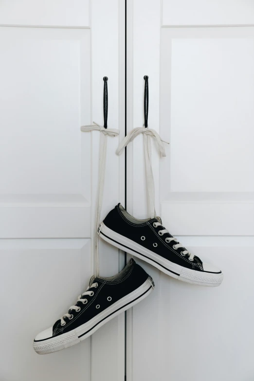 a pair of black sneakers hanging on a door, by Andries Stock, pexels contest winner, happening, with a white background, cute photo, intertwined, holiday