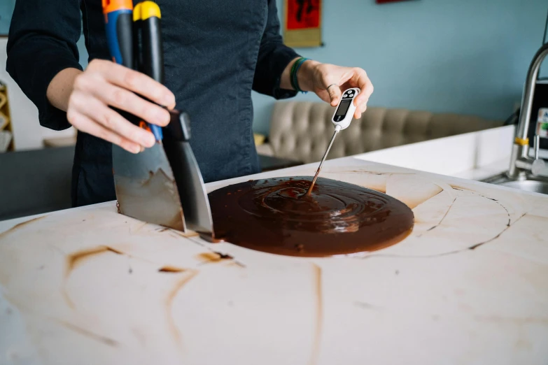 a woman is cutting a chocolate cake with a knife, a silk screen, by Julia Pishtar, pexels contest winner, process art, resin and clay art, chocolate sauce, sydney hanson, on a table