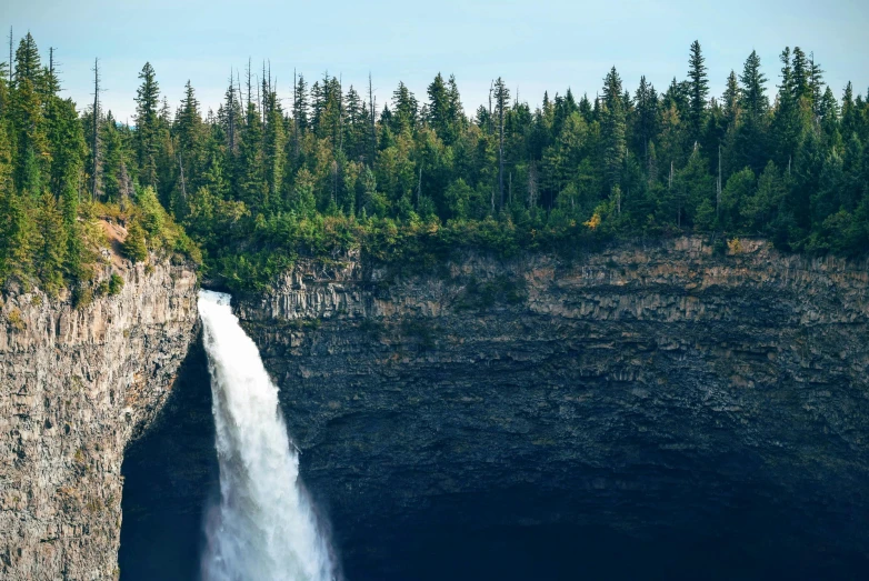 a large waterfall in the middle of a forest, by Jesper Knudsen, pexels contest winner, hurufiyya, high cliff, boreal forest, zoomed out, kimberly asstyn