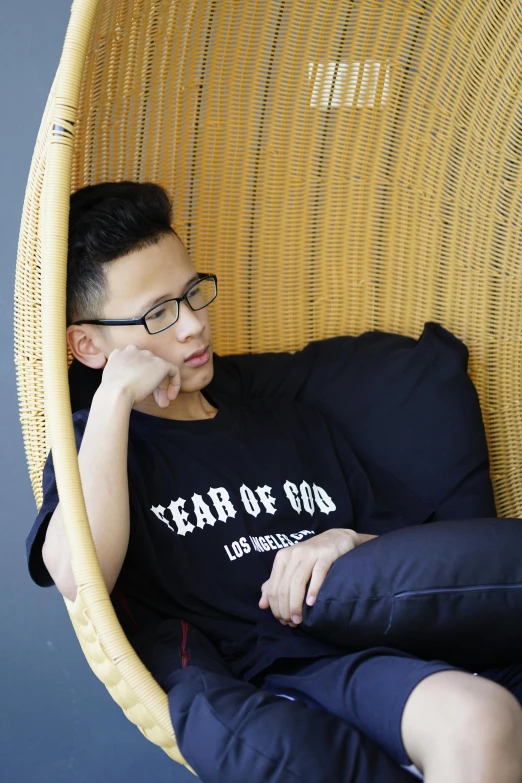 a man is sitting in a wicker chair, inspired by Lam Qua, wearing black tshirt, light of god, lgbt, wearing glasses