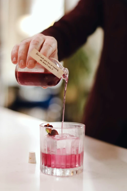 a person pouring a drink into a glass, botanicals, magenta, label, bar