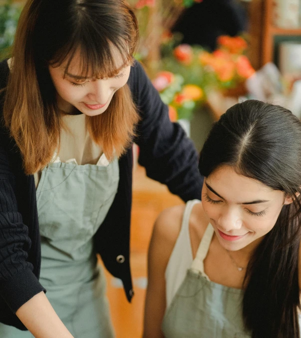 a woman standing next to a woman cutting a cake, by Robbie Trevino, trending on pexels, arts and crafts movement, young asian girl, looking from shoulder, practical, top down shot