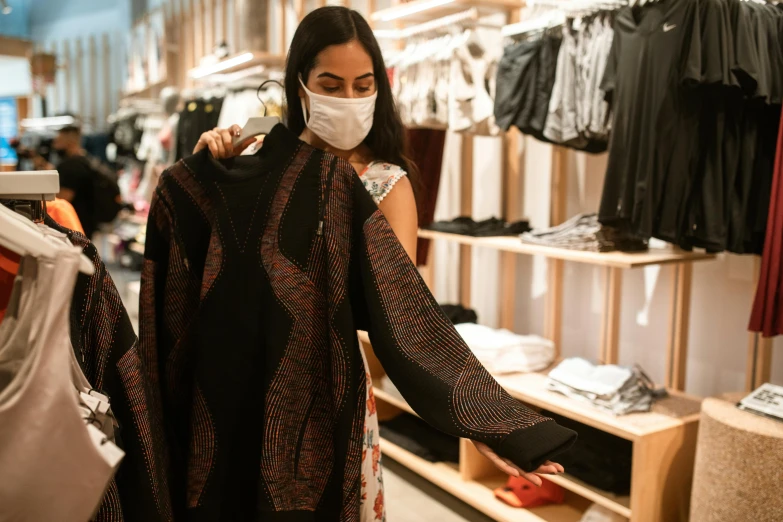 a woman wearing a face mask in a clothing store, a photo, trending on pexels, woman holding another woman, intricate clothes, alexandria ocasio - cortez, wearing nanotech honeycomb robe