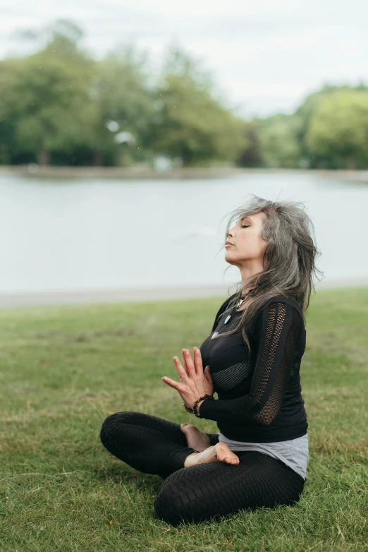 a woman sitting in the grass doing yoga, calmly conversing 8k, in a park and next to a lake, mai anh tran, praying posture