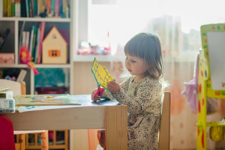 a little girl that is sitting at a table, pexels contest winner, arts and crafts movement, square, kids toys, small library, colour corrected