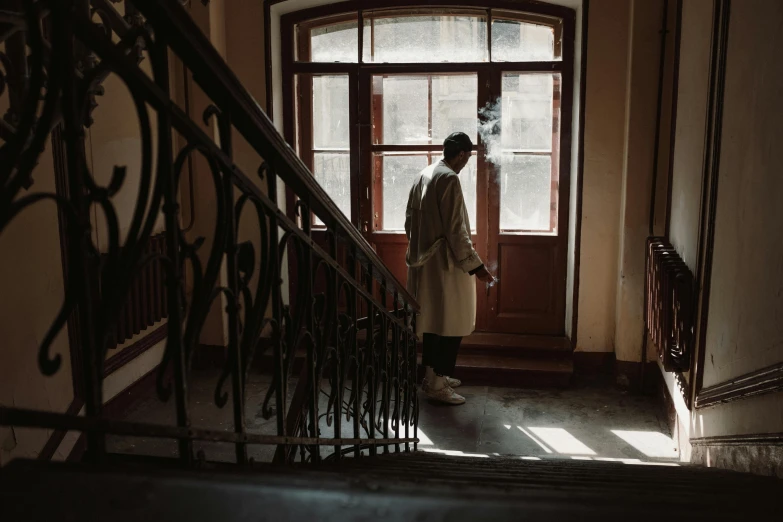 a man standing at the top of a set of stairs, inspired by Louis Stettner, pexels contest winner, light brown trenchcoat, soviet apartment, ( ( theatrical ) ), old lady