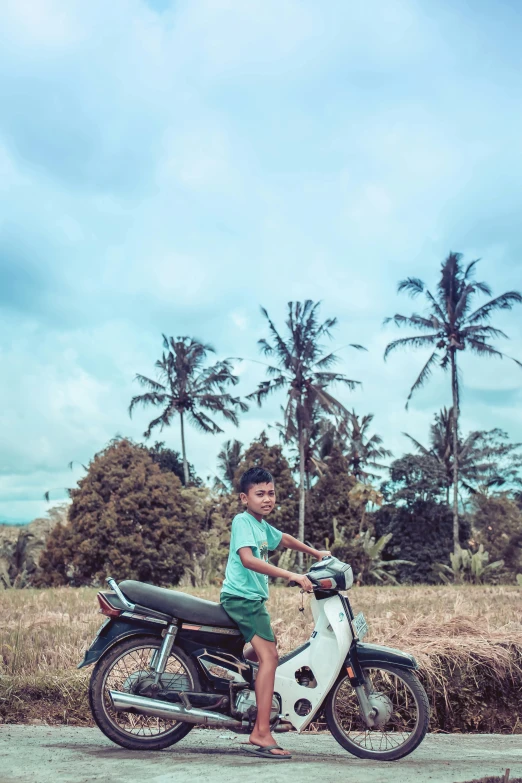 a young boy riding on the back of a motorcycle, pexels contest winner, sumatraism, a palm tree, countryside, coloured photo, square