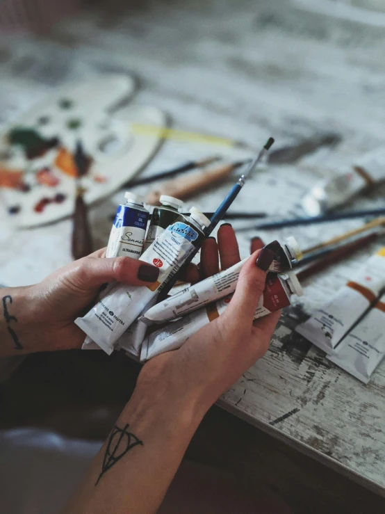 a person sitting at a table with paint and brushes, pexels contest winner, academic art, flatlay, artist wearing overalls, paint tubes, art bundle