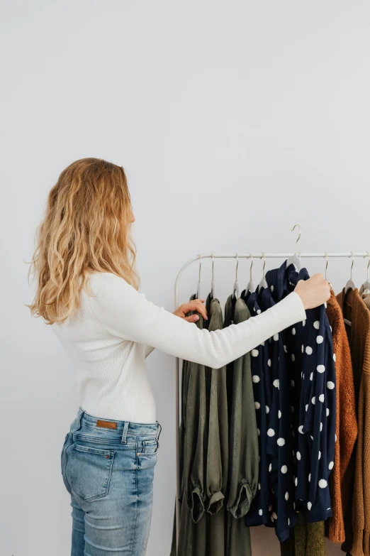 a woman standing in front of a rack of clothes, ecommerce photograph, presenting wares, green and brown clothes, in front of white back drop