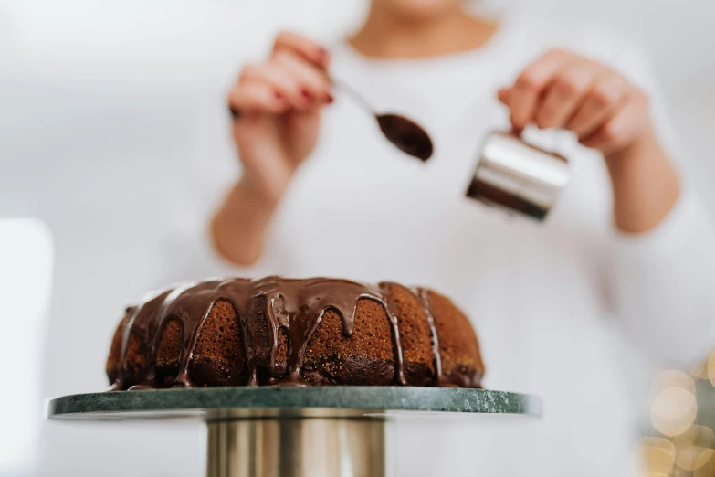 a woman sprinkles chocolate icing on a bundt cake, by Julia Pishtar, pexels contest winner, made of liquid metal and marble, rounded lines, official product photo, amanda lilleston