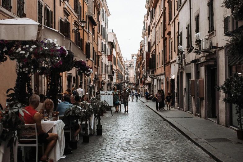 a narrow cobblestone street with people sitting at tables, by Julia Pishtar, pexels contest winner, neoclassicism, all roads lead to rome, background image, 🦩🪐🐞👩🏻🦳, proudly walking down the street