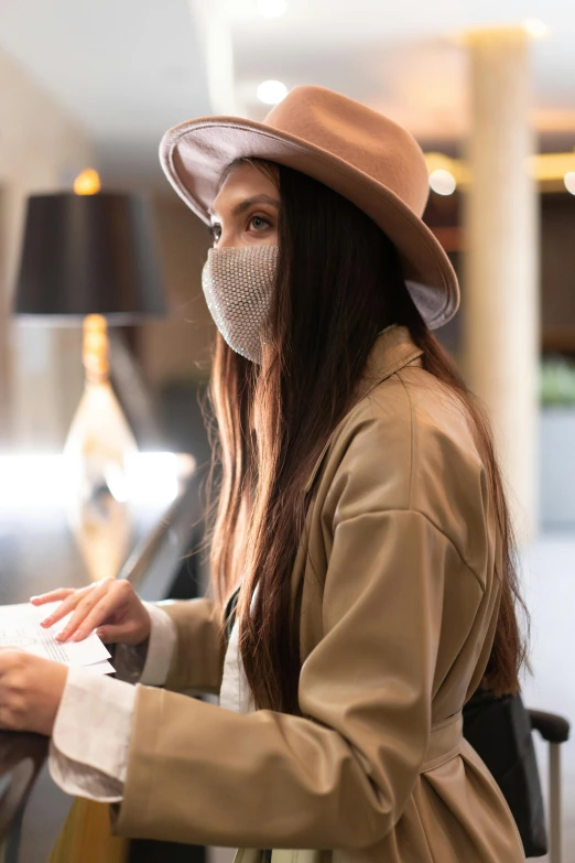 a woman wearing a face mask at an airport, a portrait, trending on pexels, beige fedora, sitting on a mocha-colored table, signing a bill, in a hotel hallway