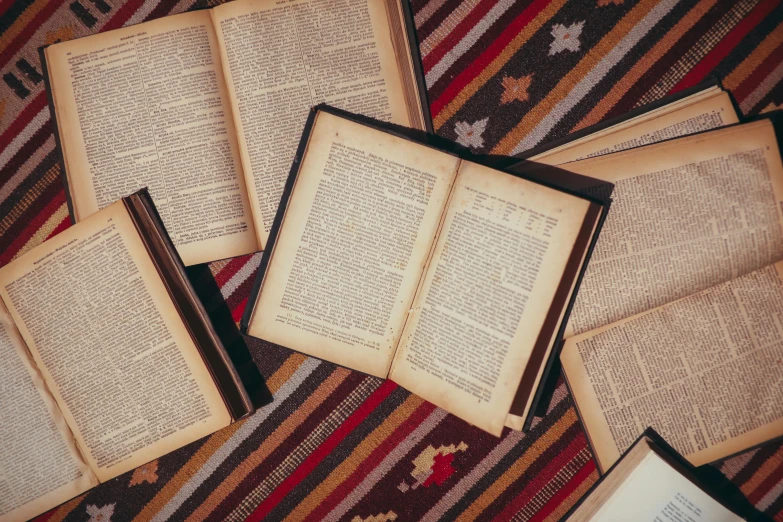 a pile of open books sitting on top of a rug, a cross stitch, trending on unsplash, arts and crafts movement, orthodox, performing, laying down, wearing brown robes