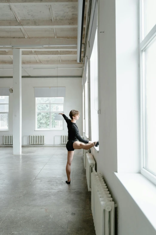 a woman standing in front of a window next to a radiator, by Elizabeth Polunin, arabesque, high kick, low quality photo, cai xukun, daniil kudriavtsev