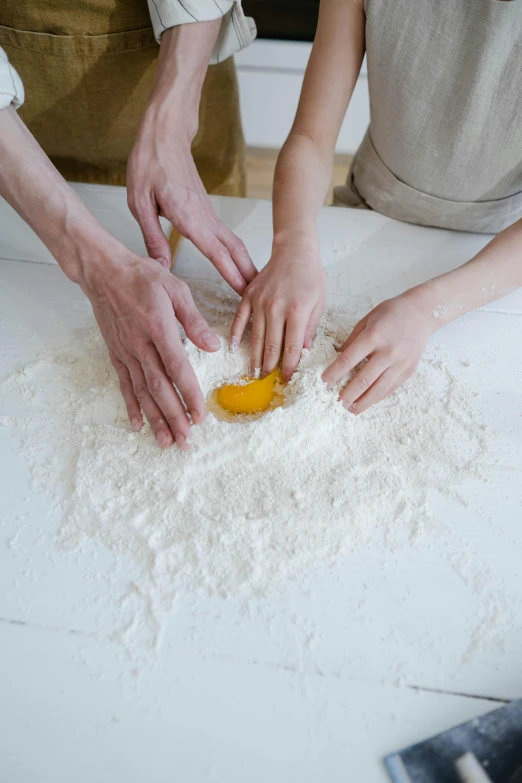 a couple of people that are making some food, hand on table, covered in white flour, raw egg yolks, spiralling