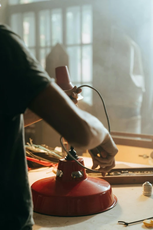 a close up of a person making something on a table, an airbrush painting, by William Berra, pexels contest winner, red smoke coming from lamp, small hipster coffee shop, tools, midcentury modern