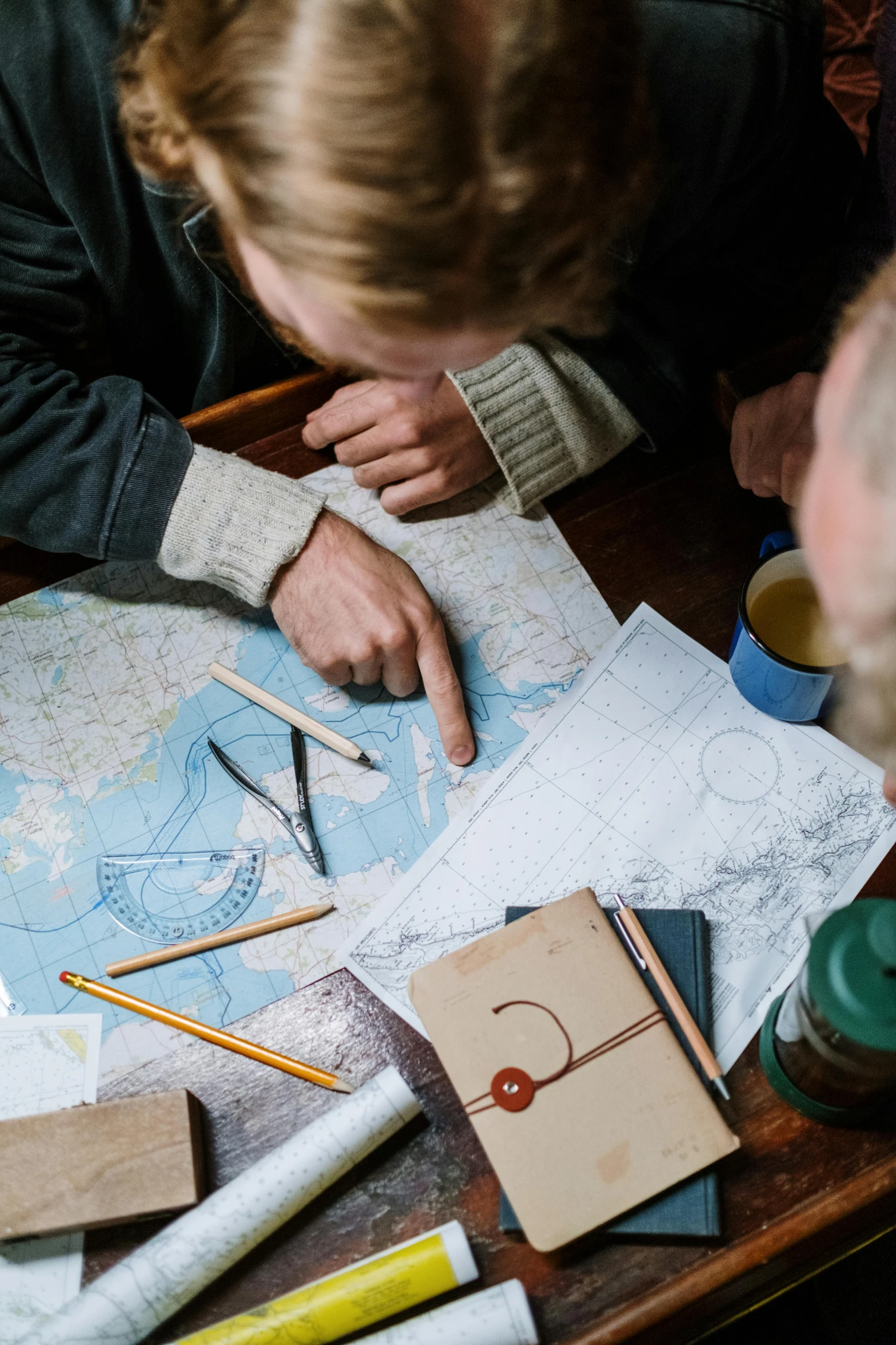 a couple of people that are looking at a map, by Jan Tengnagel, trending on unsplash, food. craft and adventure, ocean dept, sketching, on a wooden desk