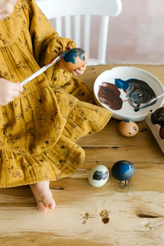 a little girl sitting on top of a wooden table, process art, holding a golden bell, mini planets, ochre, full product shot