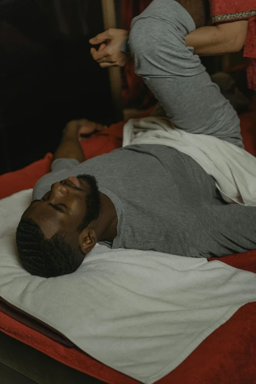 a man laying on a bed in a room, red cloth around his shoulders, jaylen brown, healing through motion, gray men