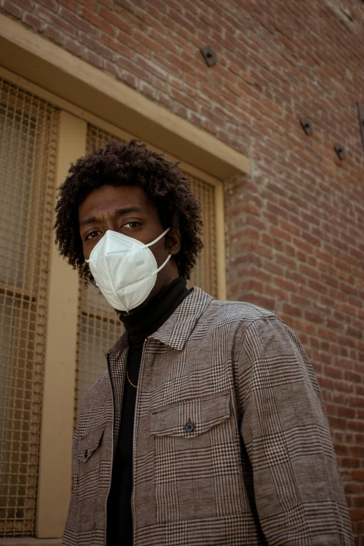 a man wearing a face mask in front of a brick building, an album cover, trending on pexels, respirator, brown skinned, looking away from camera, puffy