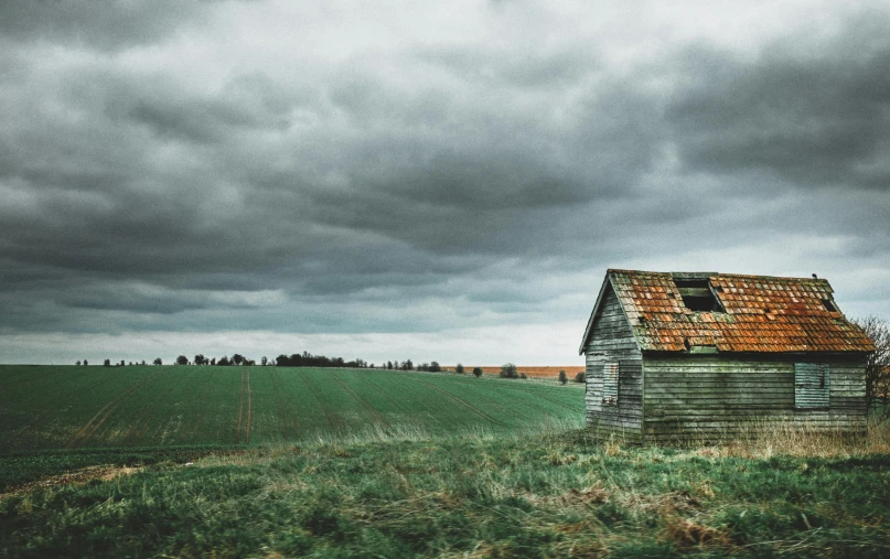 an old barn in a field under a cloudy sky, an album cover, unsplash contest winner, background image, makeshift house, colourised, overcast