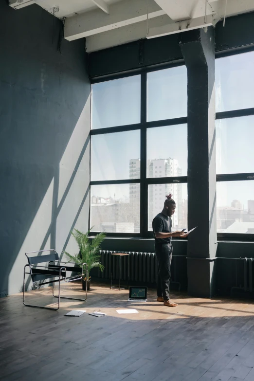 a man standing in front of a window with a laptop, unsplash contest winner, modernism, interior of a loft, behance lemanoosh, black windows, full sun