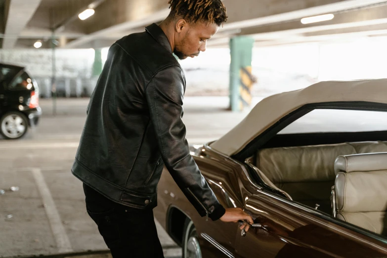 a man standing next to a car in a parking garage, trending on pexels, leather clothing, thumbnail, liquid gold, profile image
