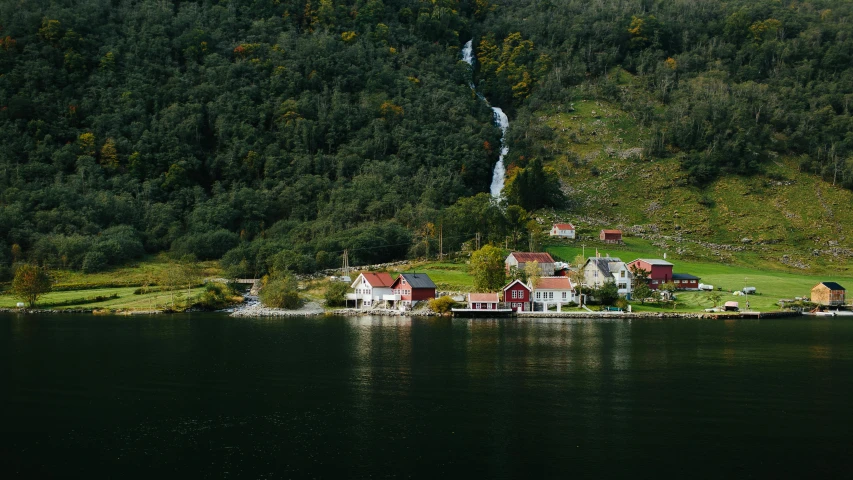 a group of houses sitting on top of a lush green hillside, by Jesper Knudsen, pexels contest winner, hurufiyya, waterfall falling into a lake, autum, fjord, subtle detailing