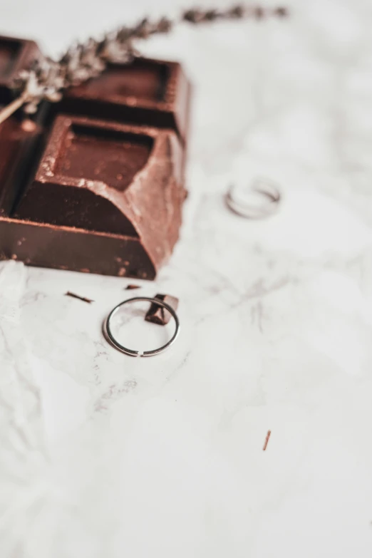 a piece of chocolate sitting on top of a table, inspired by Pieter de Ring, trending on unsplash, wearing two metallic rings, love story, silver details, while marble