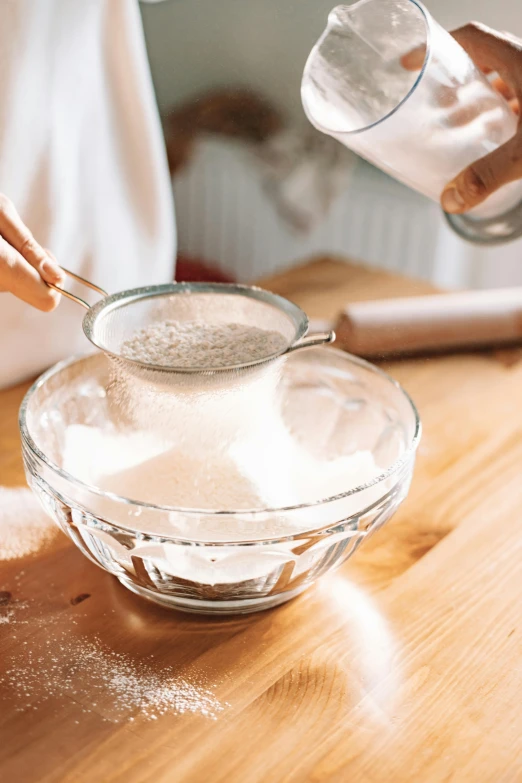 a person pouring salt into a bowl on top of a wooden table, by Lucette Barker, trending on pexels, powdered sugar, on kitchen table, thumbnail, seasonal