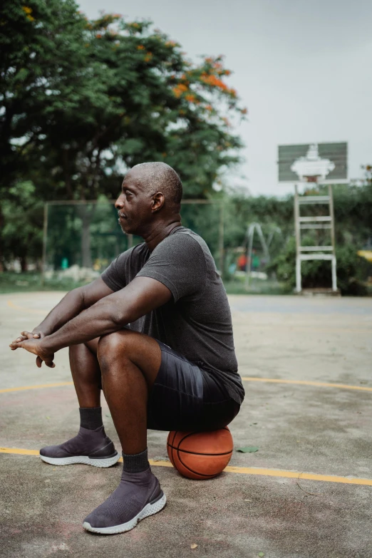 a man sitting on top of a basketball ball, profile image, on the concrete ground, lance reddick, basketball court