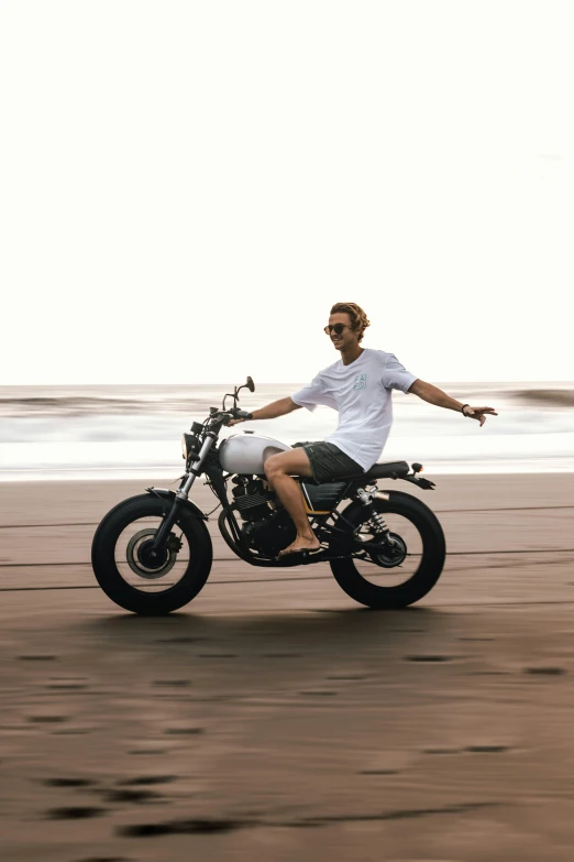 a man riding a motorcycle on top of a sandy beach, wearing a linen shirt, streetwear, hair, bali